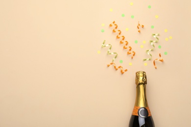 Photo of Bottle with champagne and shiny confetti on beige background, flat lay. Space for text