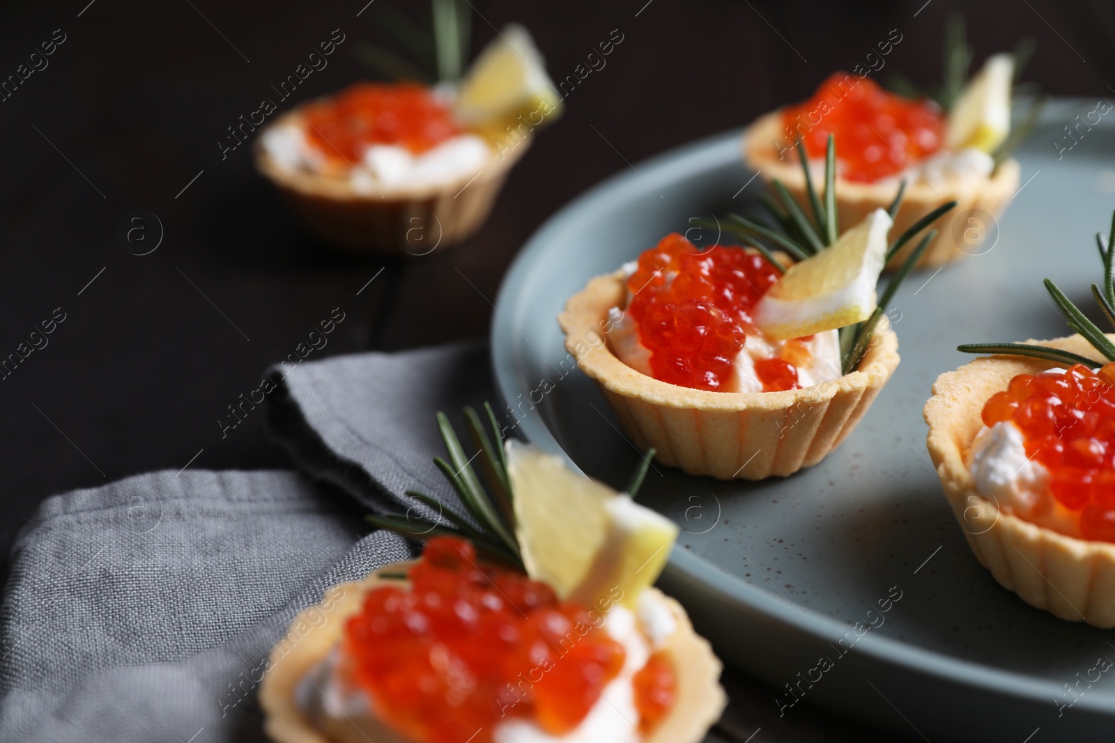 Photo of Delicious tartlets with red caviar and cream cheese served on wooden table, closeup