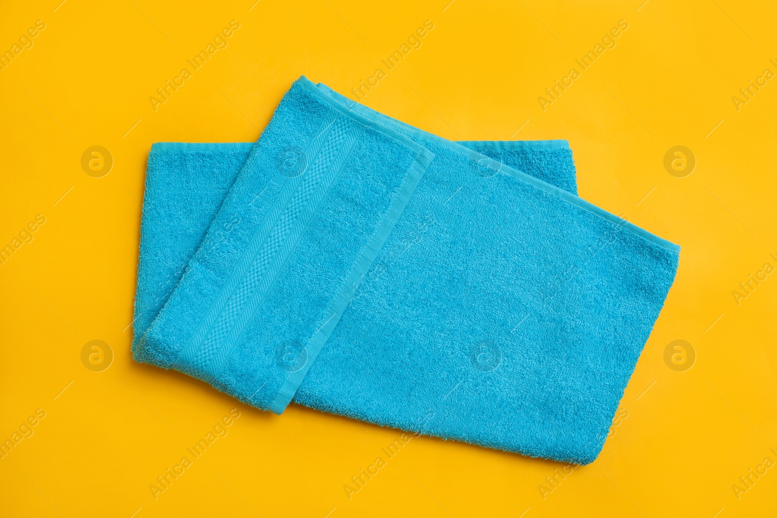 Photo of Folded light blue beach towel on yellow background, top view