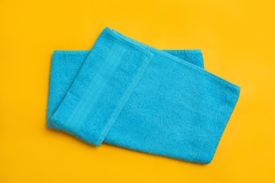 Photo of Folded light blue beach towel on yellow background, top view