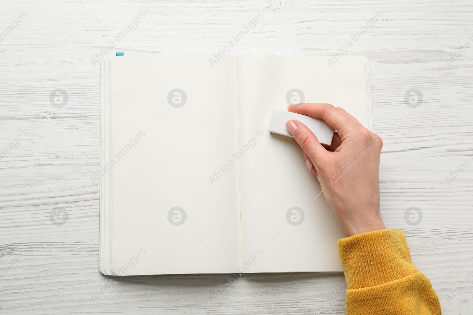 Photo of Woman erasing something in notebook at white wooden table, closeup