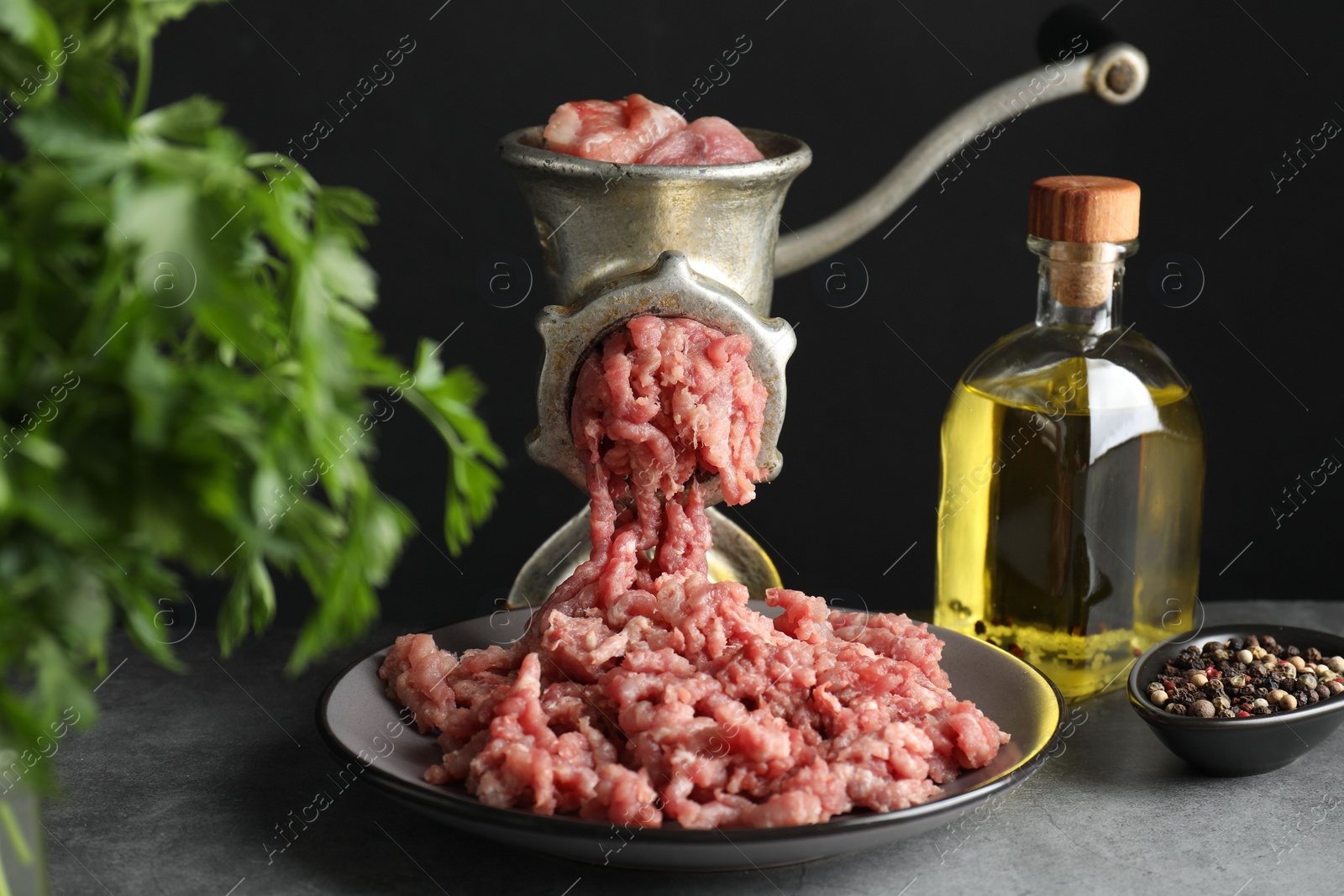 Photo of Manual meat grinder with beef mince, spices, oil and parsley on grey table