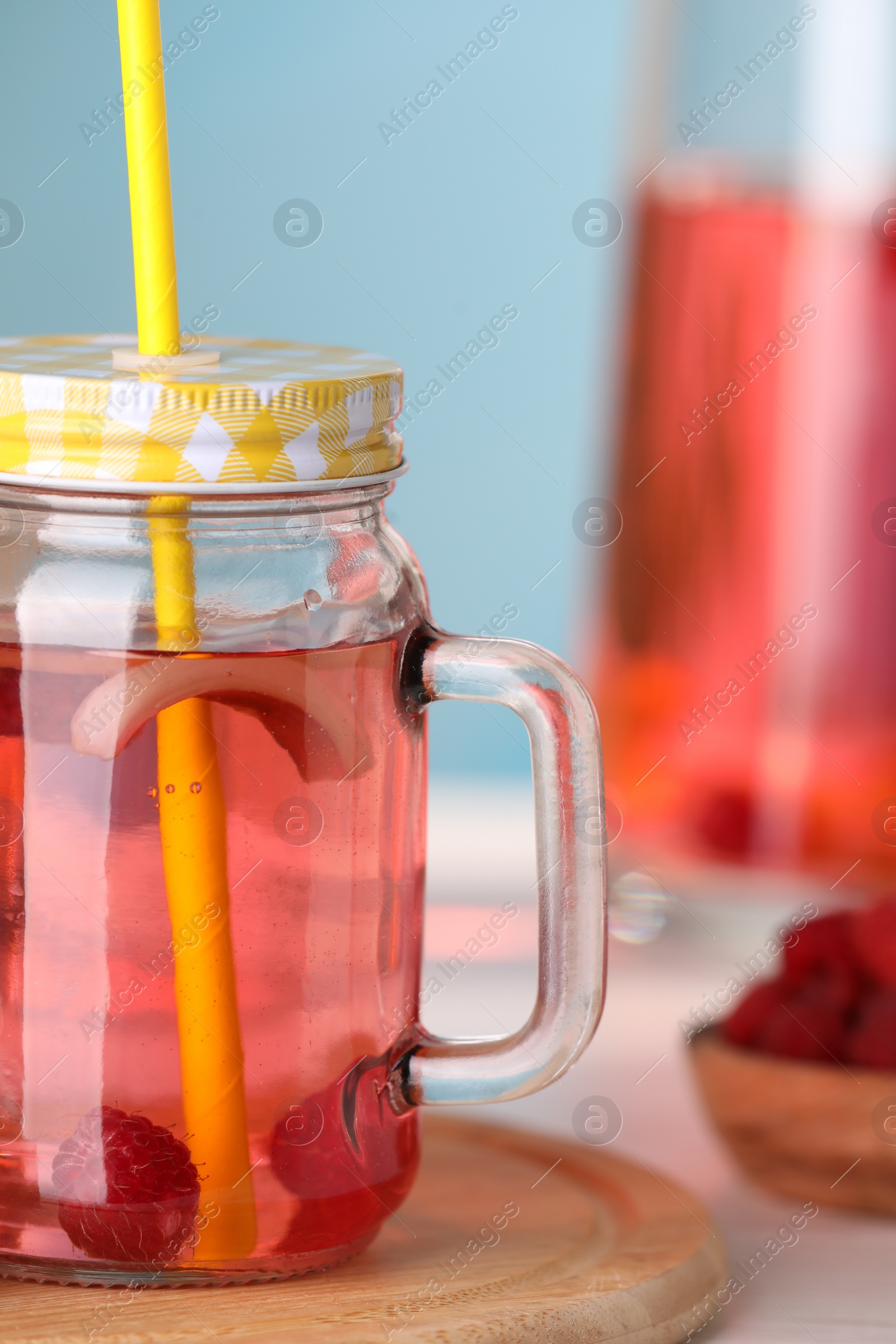 Photo of Mason jar of tasty rhubarb cocktail with raspberry on table, closeup