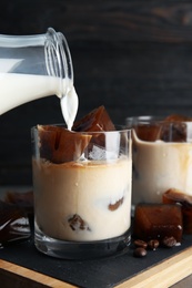 Pouring milk into glass with coffee ice cubes on table