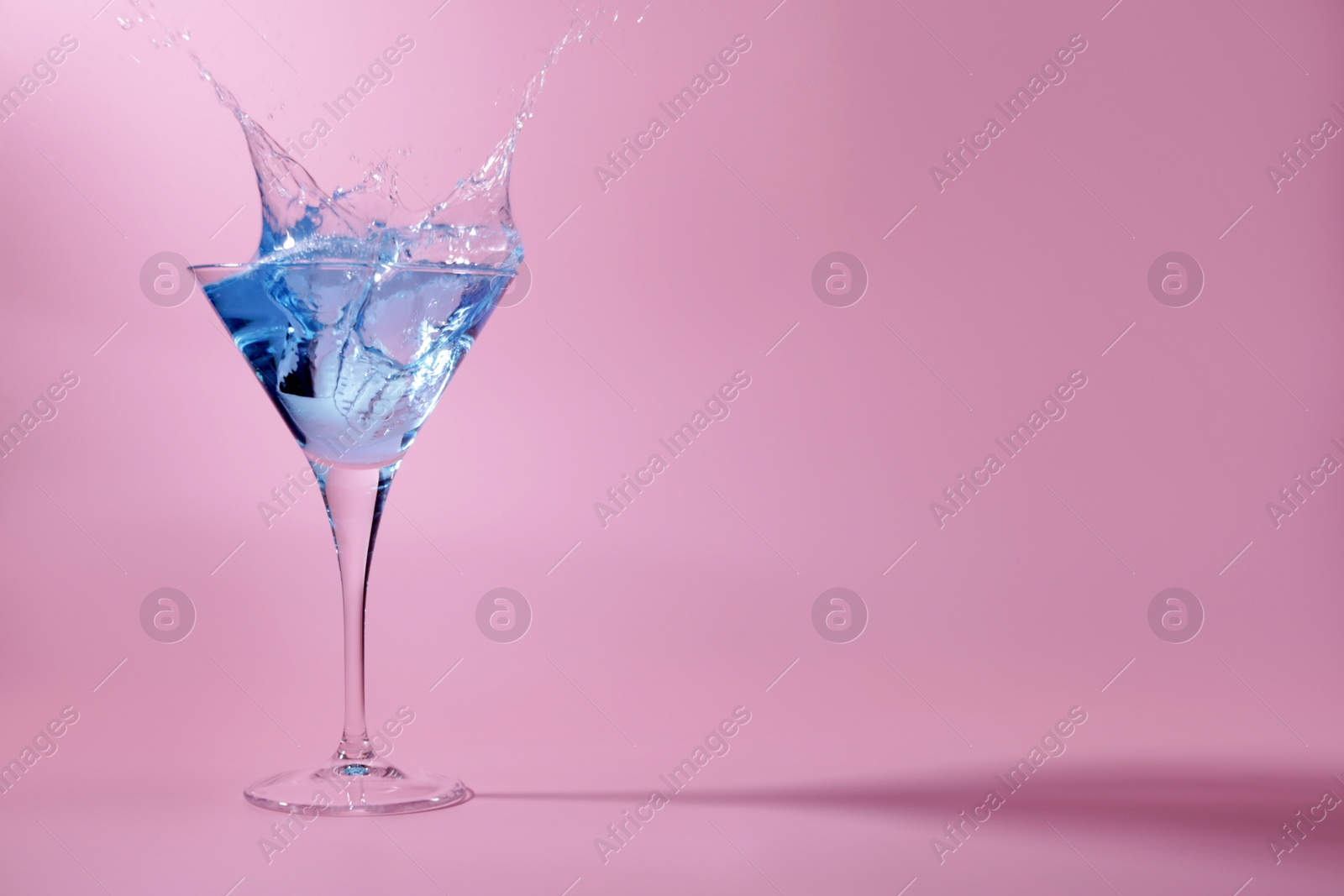 Photo of Cocktail splashing out of martini glass on pink background, space for text