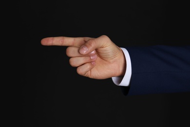 Businessman pointing at something on black background, closeup. Finger gesture