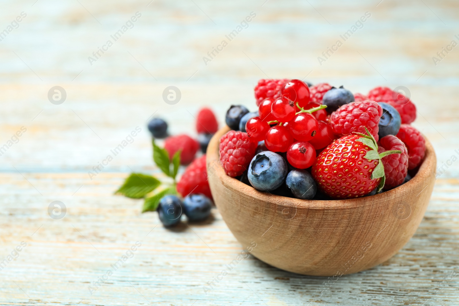 Photo of Mix of different fresh berries in bowl on wooden table. Space for text