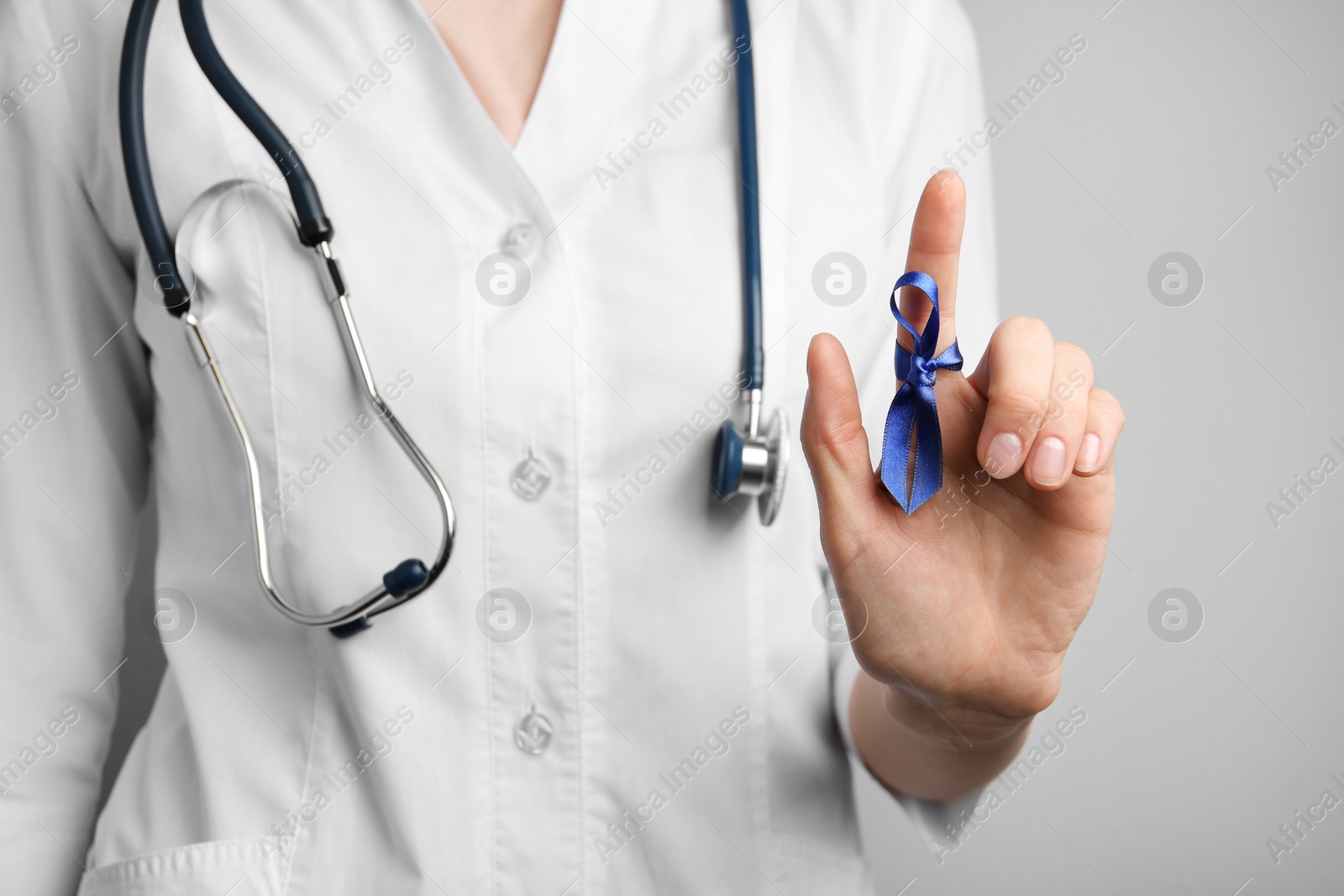 Photo of Doctor with blue awareness ribbon on finger, closeup. Symbol of medical issues