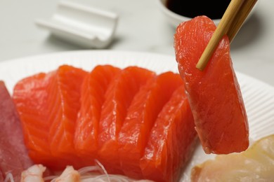 Photo of Taking tasty salmon slice with chopsticks from plate, closeup. Delicious sashimi dish