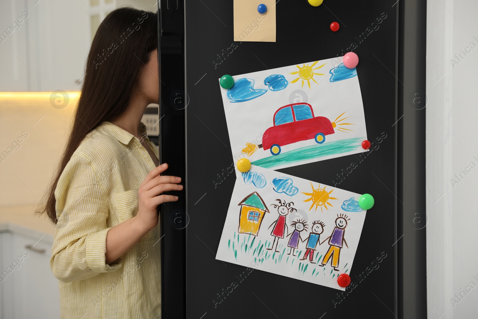 Photo of Woman near refrigerator with child's drawings in kitchen, closeup