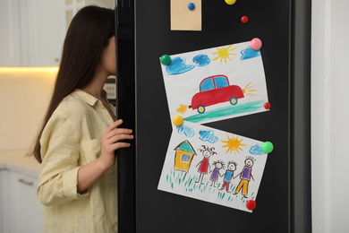 Photo of Woman near refrigerator with child's drawings in kitchen, closeup