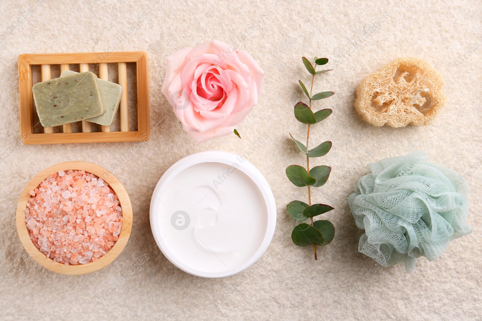 Photo of Flat lay composition with moisturizing cream in open jar and other body care products on light textured table