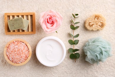 Photo of Flat lay composition with moisturizing cream in open jar and other body care products on light textured table