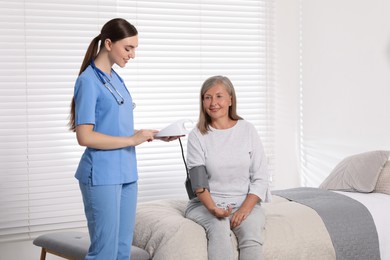 Young healthcare worker measuring senior woman's blood pressure indoors