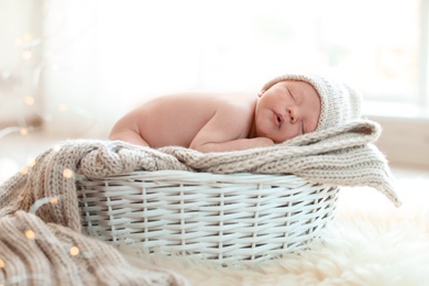 Photo of Adorable newborn baby lying in basket with knitted plaid indoors