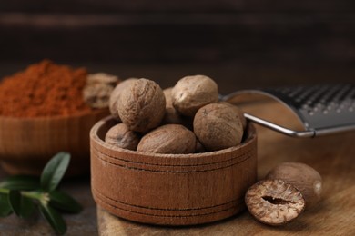 Photo of Nutmegs in wooden bowl and grater on table