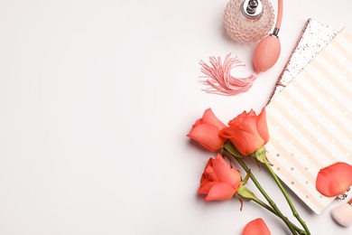 Photo of Flat lay composition with coral roses, notebooks and perfume bottle on white background. Space for text