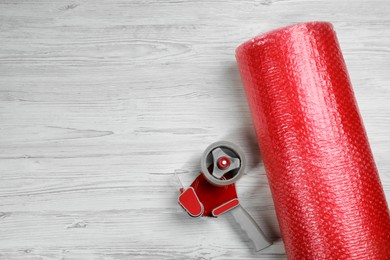 Bubble wrap roll and tape dispenser on white wooden background, flat lay. Space for text