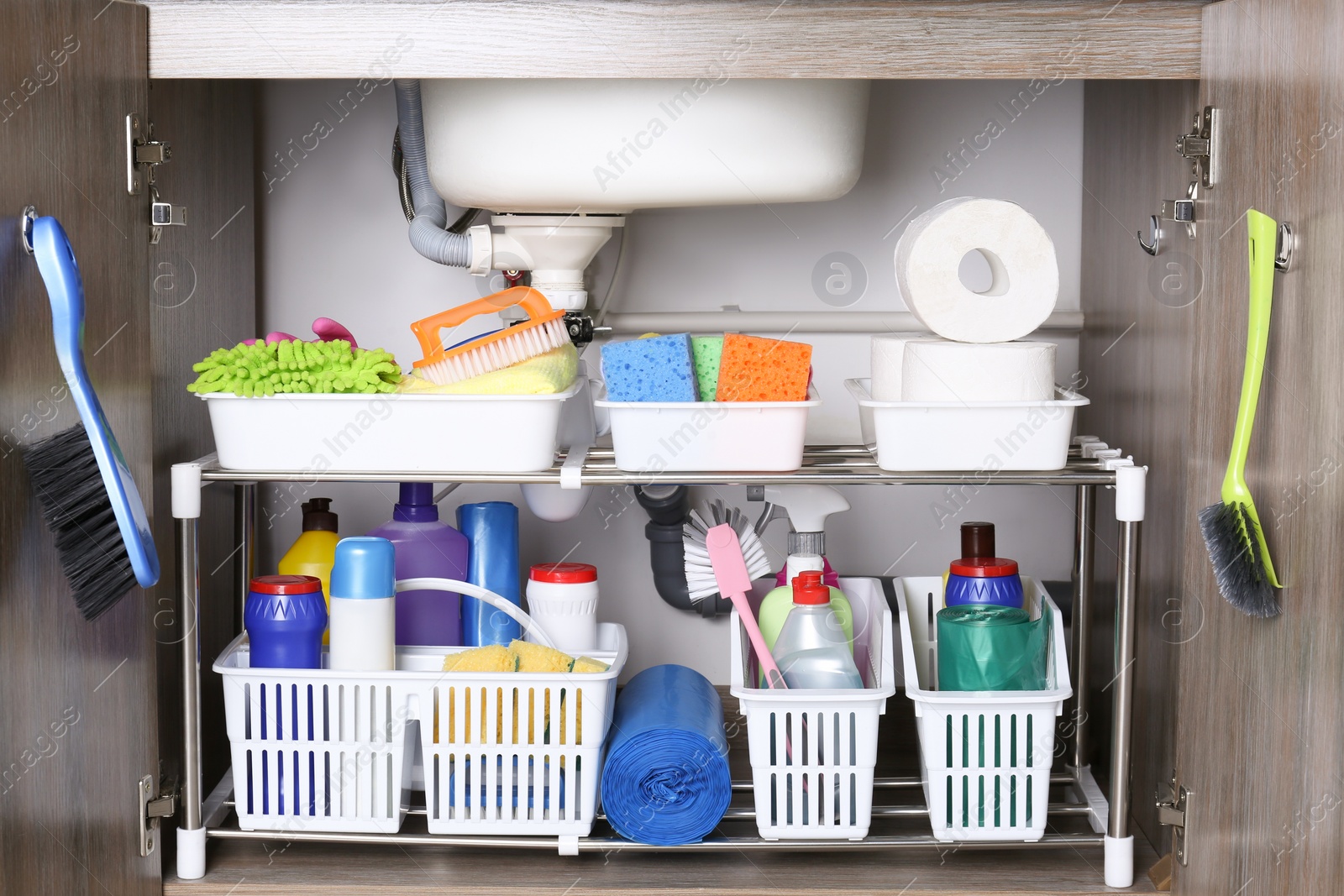 Photo of Open under sink cabinet with different cleaning supplies in kitchen