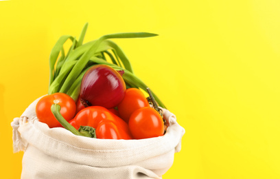 Photo of Cotton eco bag with vegetables on yellow background, closeup. Space for text
