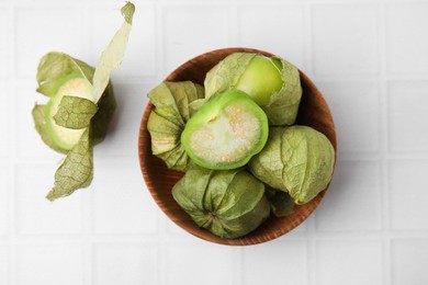 Photo of Fresh green tomatillos with husk in bowl on white tiled table, top view