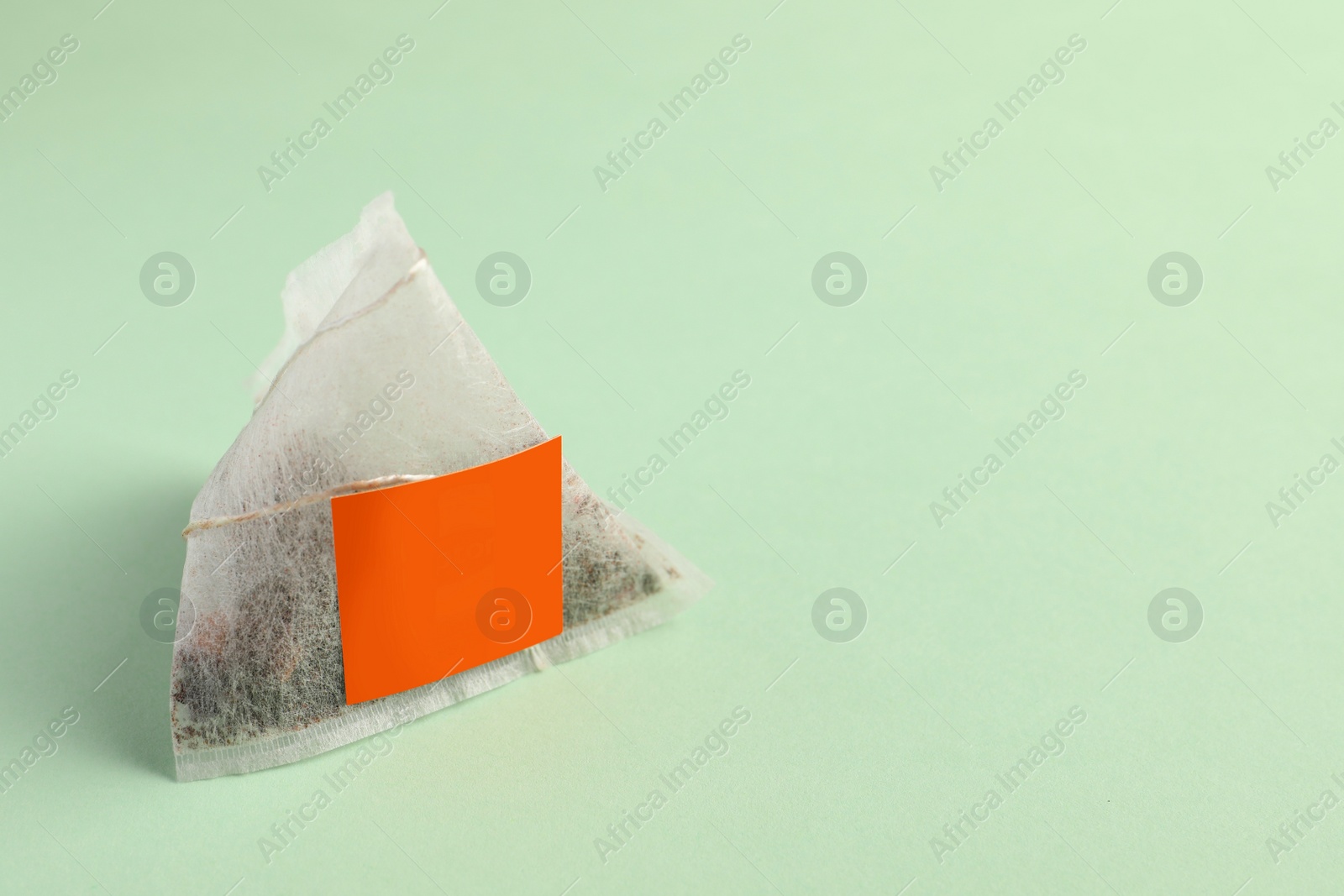 Photo of New tea bag with tab on light green background, closeup. Space for text