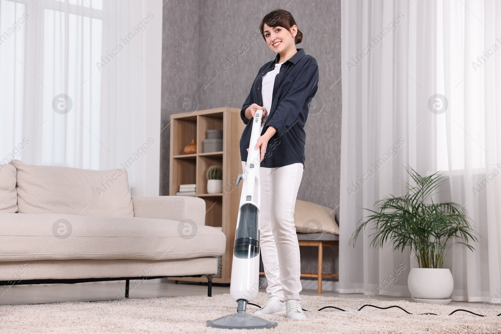 Photo of Happy young housewife vacuuming carpet at home