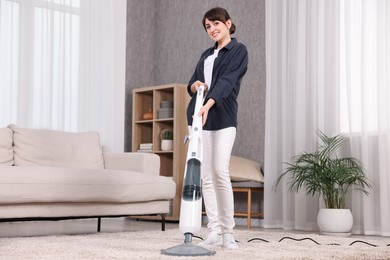 Happy young housewife vacuuming carpet at home