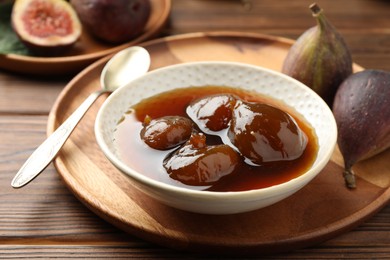 Photo of Bowl of tasty sweet jam and fresh figs on wooden table