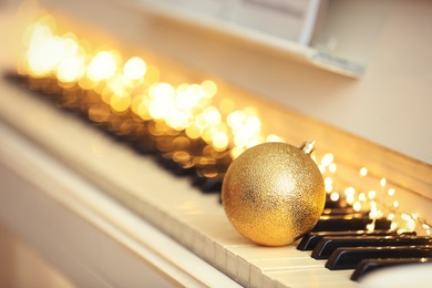 Beautiful golden bauble and fairy lights on piano keys, space for text. Christmas music