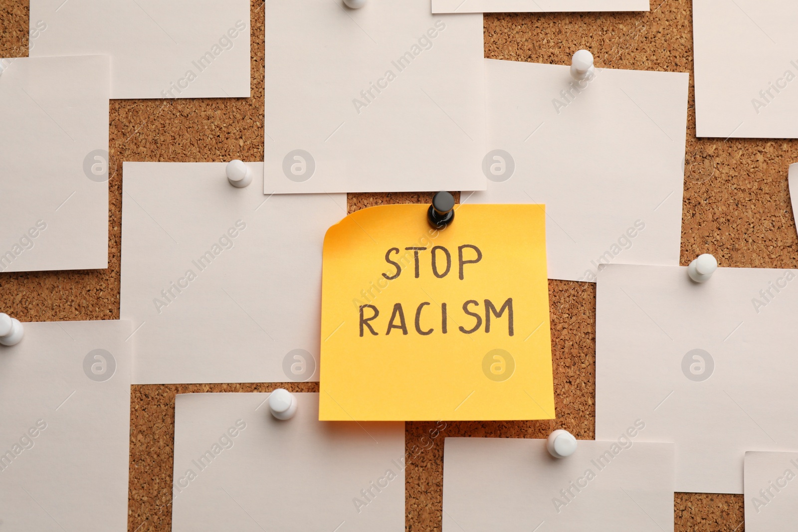 Photo of Yellow paper note with phrase Stop Racism among white ones attached to cork board