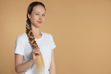 Teenage girl with strong healthy braided hair on beige background, space for text