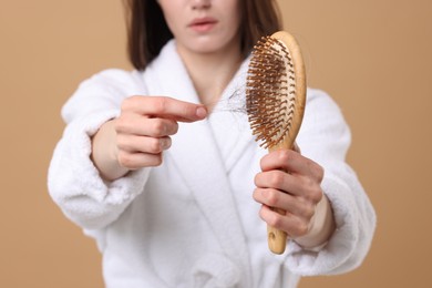 Photo of Woman taking her lost hair from brush on light brown background, closeup. Alopecia problem