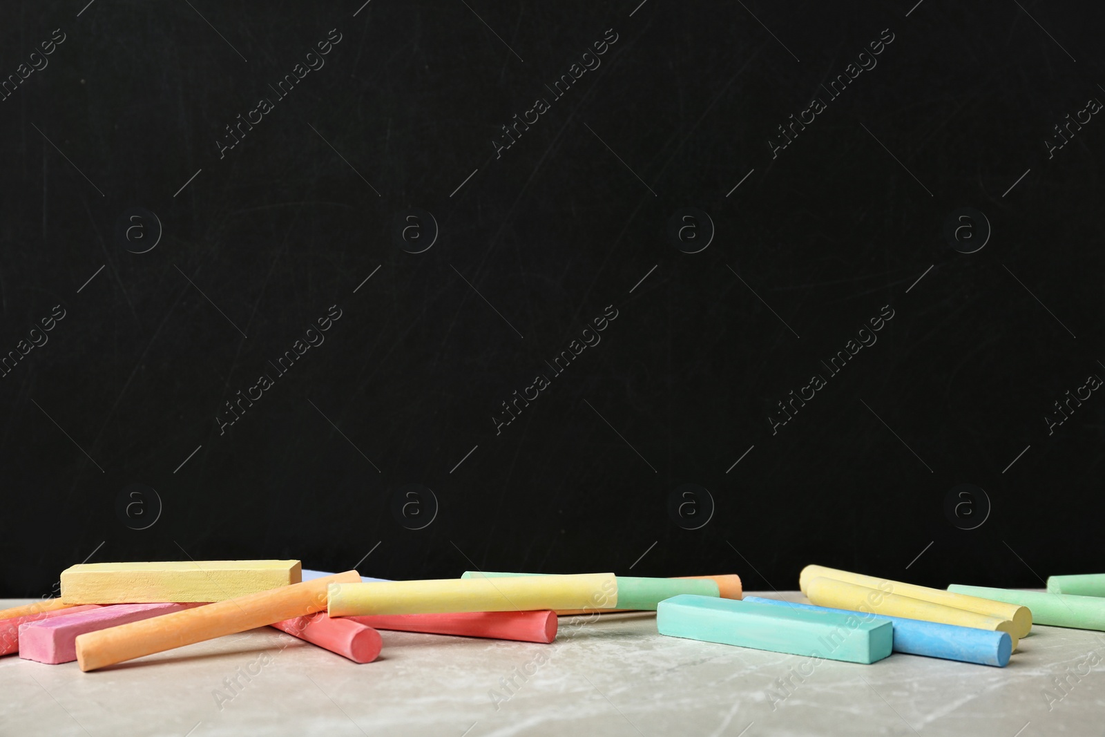 Photo of Color pieces of chalk on table near blackboard