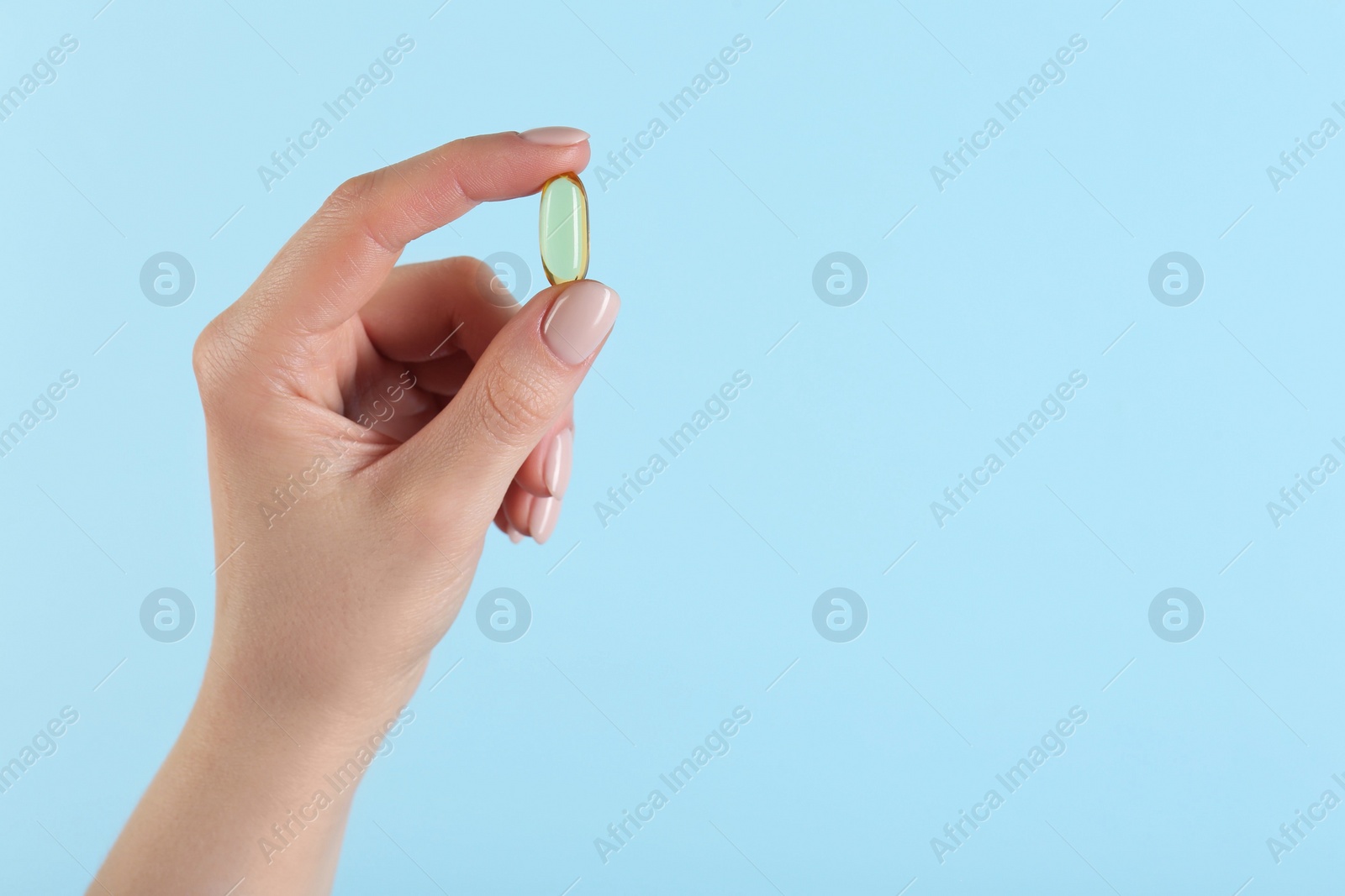 Photo of Woman holding vitamin capsule on light blue background, closeup with space for text. Health supplement