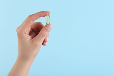 Photo of Woman holding vitamin capsule on light blue background, closeup with space for text. Health supplement