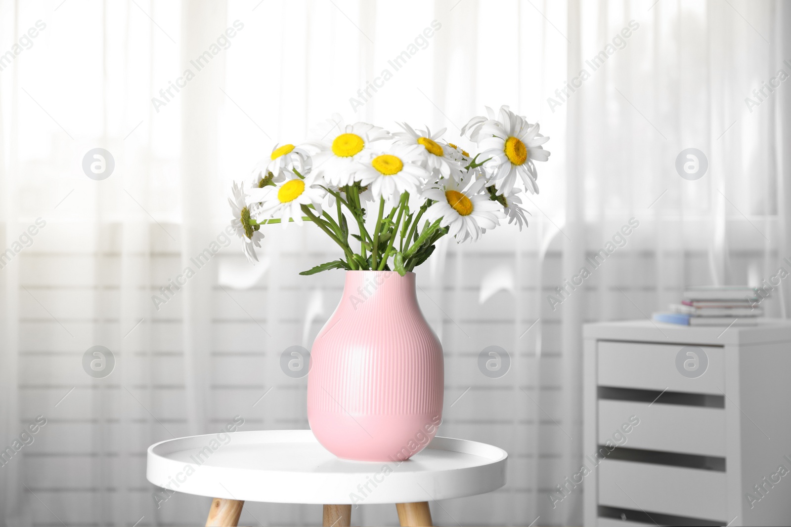 Photo of Vase with beautiful chamomile flowers on table in room