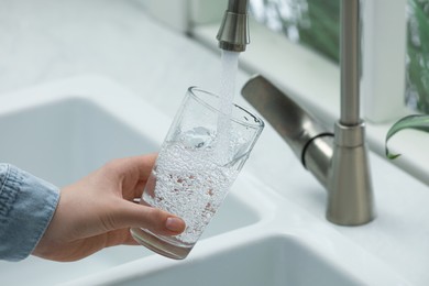 Woman filling glass with water from tap at home, closeup