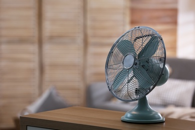 Photo of Modern electric fan on wooden table indoors. Space for text