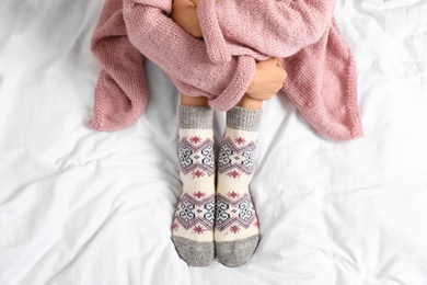 Woman wearing knitted socks on white fabric, top view. Warm clothes