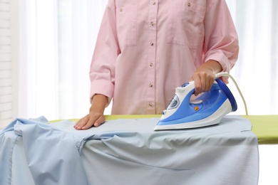 Photo of Young woman ironing clean shirt at home, closeup. Laundry day