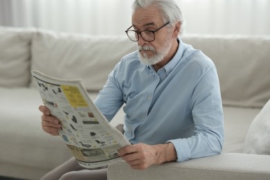 Photo of Portrait of grandpa with stylish glasses reading newspaper on sofa indoors