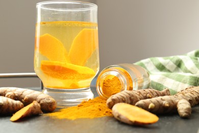 Glass cup of tasty tea, turmeric roots and powder on black textured table