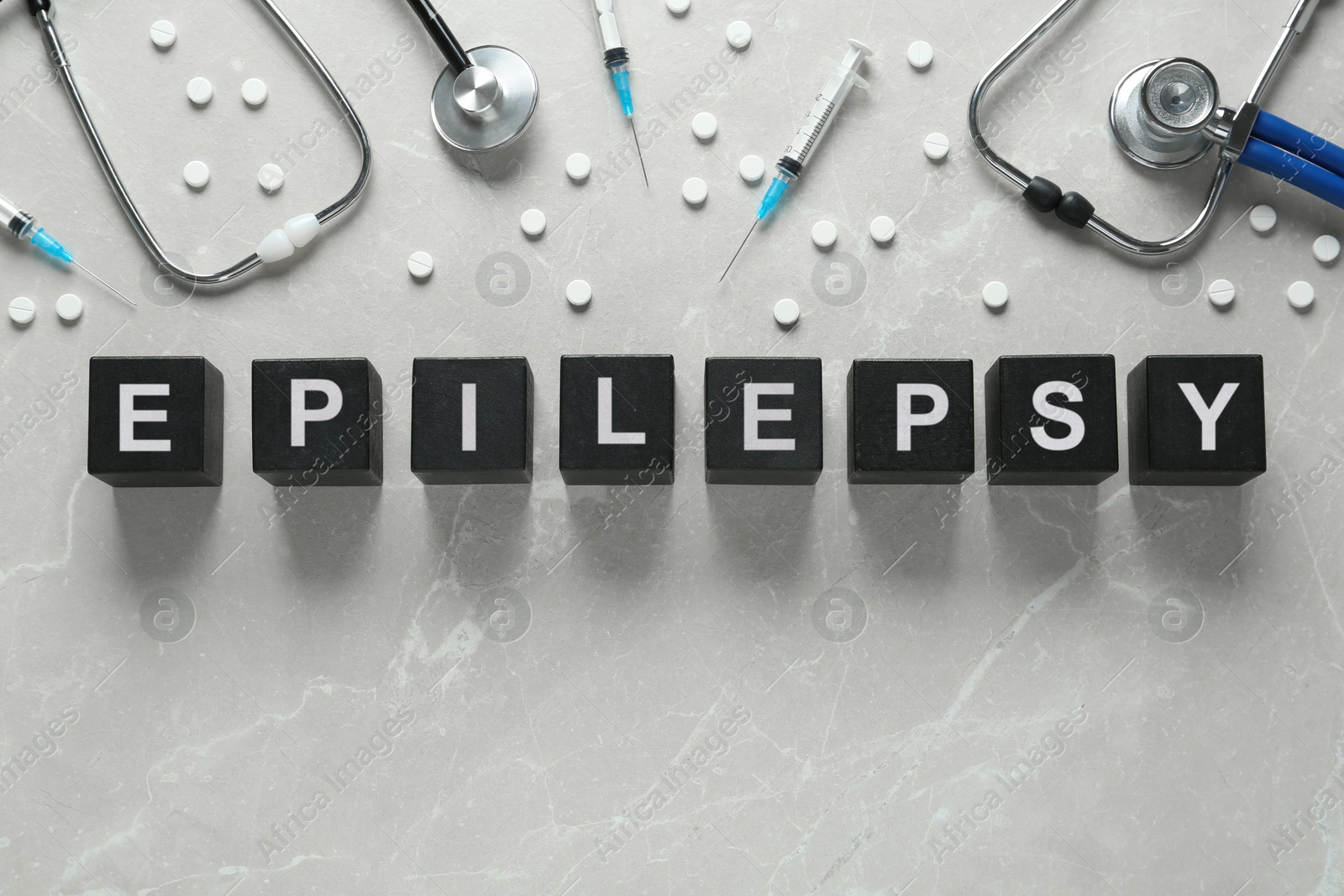 Photo of Black cubes with word Epilepsy, stethoscopes, pills and syringes on light grey table, flat lay