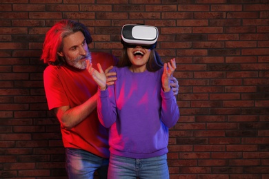 Emotional woman playing video games with VR headset and mature man near brick wall