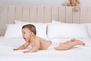 Cute baby in dry soft diaper on white bed at home