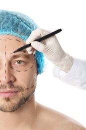 Doctor drawing marks on man's face for cosmetic surgery operation against white background, closeup