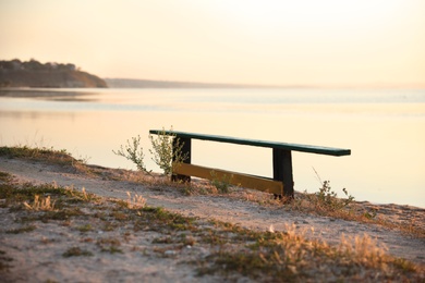 Photo of Wooden bench near river at sunrise. Early morning landscape