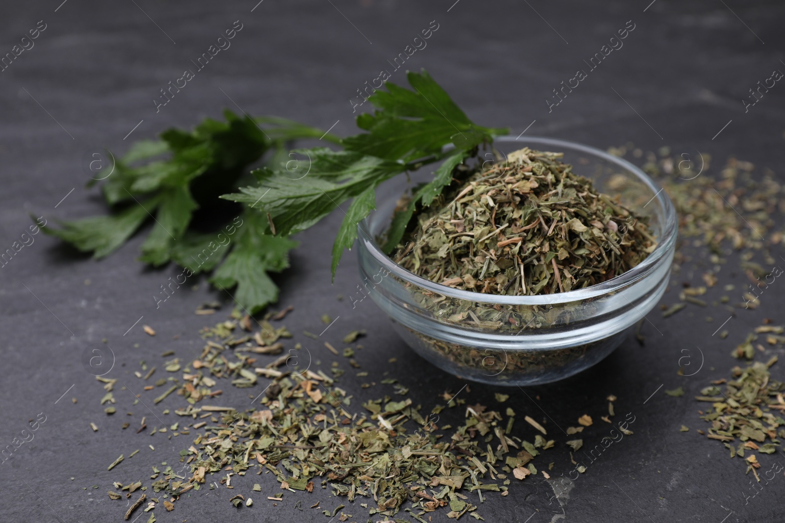 Photo of Dried parsley and fresh leaves on black table, closeup