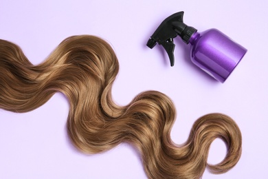 Lock of brown wavy hair and spray bottle on color background, flat lay